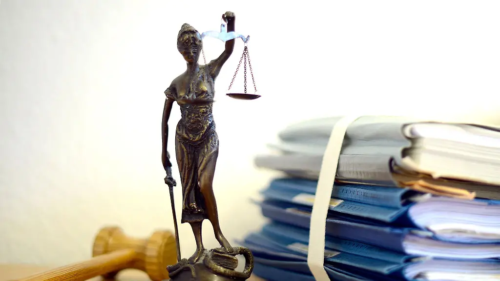 Die-modellhafte-Nachbildung-der-Justitia-steht-in-einem-Raum-eines-Richters-neben-einem-Holzhammer-und-einem-Aktenstapel