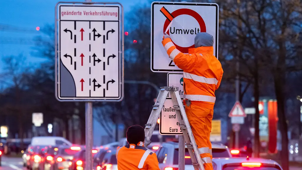 Arbeiter-entfernen-einen-roten-Klebestreifen-von-einem-Schild-mit-der-Aufschrift-Umwelt-Zone-und-Diesel-ausser-Lieferverkehr-und-Anwohner-erst-ab-Euro-5-V