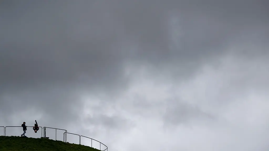 Dunkle-Wolken-ziehen-im-Olympiapark-ueber-den-Olympiaberg-auf-dem-trotz-des-trueben-Wetters-einige-Ausfluegler-stehen