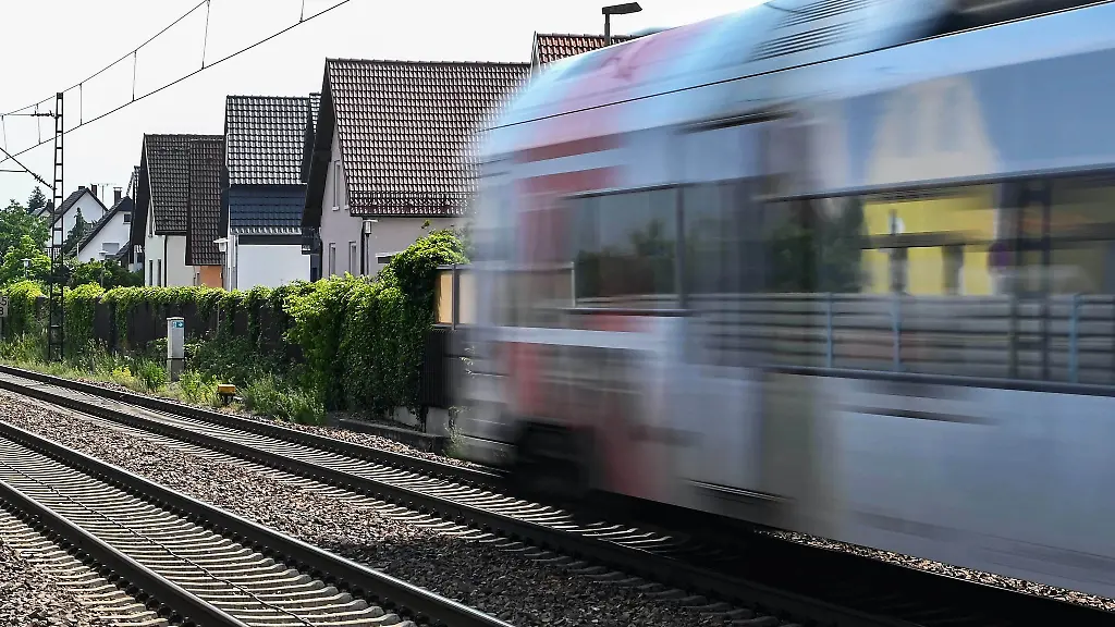 Auf-der-Bahnstrecke-Karlsruhe-Mannheim-faehrt-ein-Zug-an-Haeusern-vorbei-Der-Laerm-von-Zuegen-gilt-als-bedeutende-Laermquelle-in-Deutschland