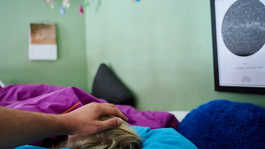 Ein-Vater-legt-seine-Hand-auf-den-Kopf-eines-Kindes-das-im-Bett-liegt