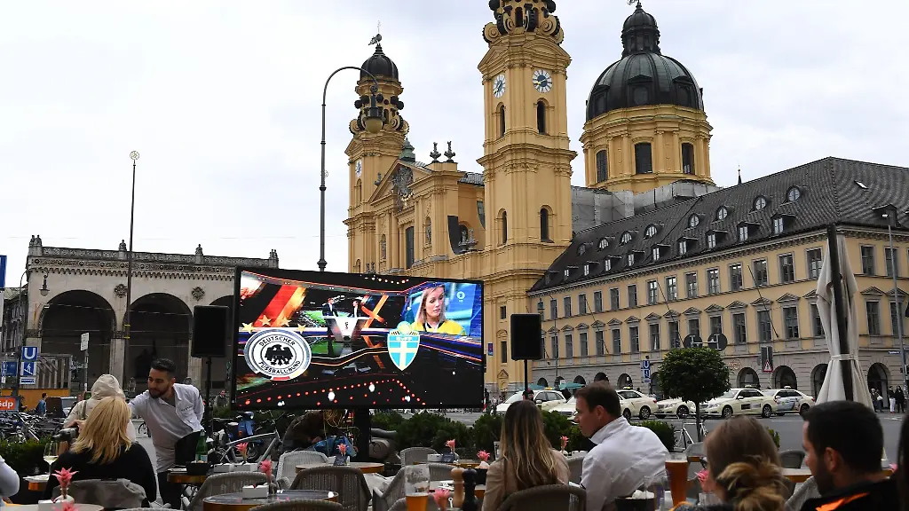 Ein-grosser-Bildschirm-steht-vor-den-Stuehlen-des-Cafehaus-Tambosi-um-die-Uebertragung-des-Fussballspiels-Deutschland-Schweden-bei-der-Fussball-Weltmeisterschaft-unter-freiem-Himmel-auf-dem-Odeonsplatz-vor-der-Theatinerkirche-sehen-zu-koennen