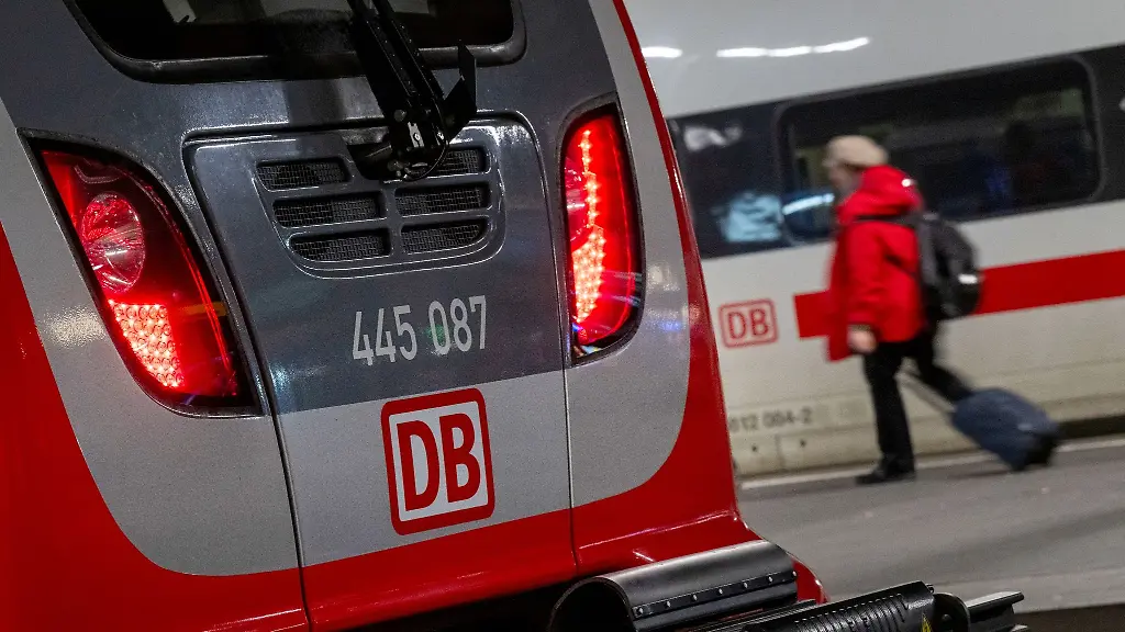 Eine-Regionalbahn-und-ein-ICE-der-Deutschen-Bahn-stehen-nebeneinander-im-Hauptbahnhof-waehrend-eine-Frau-mit-einem-Koffer-vorbeilaeuft