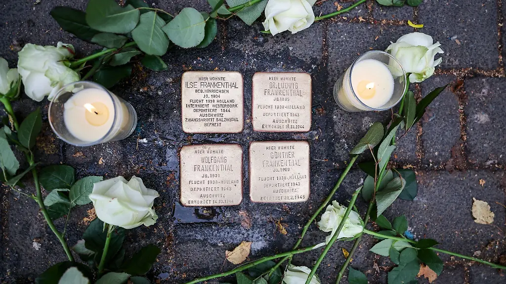 Weisse-Rosen-und-Kerzen-liegen-neben-Stolpersteinen