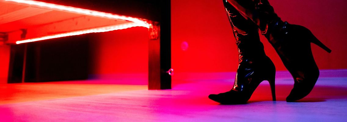 Eine Prostituierte steht vor einem rot beleuchteten Bett in einem Studio.