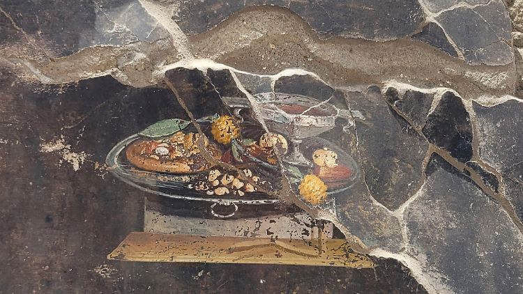 Fladenbrot, drapiert mit Früchten und einer Art Pesto, dazu ein Weinkelch: Forscher sehen darin einen frühen Vorgänger der heutigen Pizza. 
