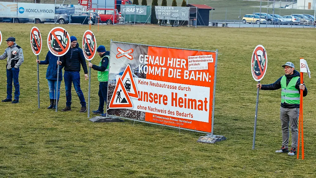 Gegner-der-geplanten-Bahntrasse-stehen-mit-Schildern-auf-einem-Sportplatz-welcher-der-Strecke-weichen-muesste