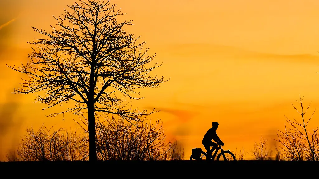 Ein-Mann-faehrt-bei-Sonnenaufgang-mit-einem-Fahrrad-ueber-einen-Feldweg-in-der-Region-Hannover