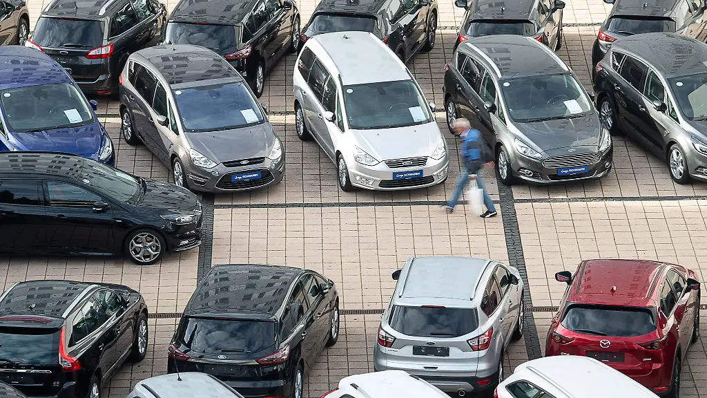 Ein-Mann-geht-in-einem-Autohaus-an-Gebrauchtwagen-vorbei