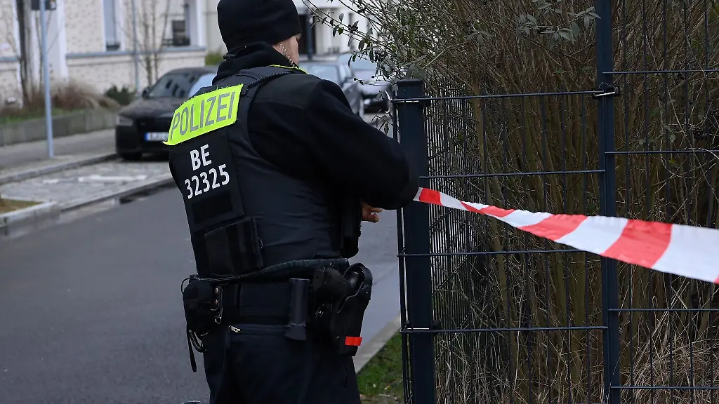 Ein-Polizist-befestigt-ein-Absperrband-an-einem-Zaun-in-Schmargendorf