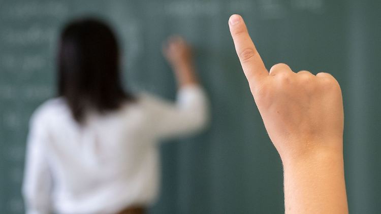 Ein Schüler meldet sich, während die Lehrerin an die Tafel schreibt.