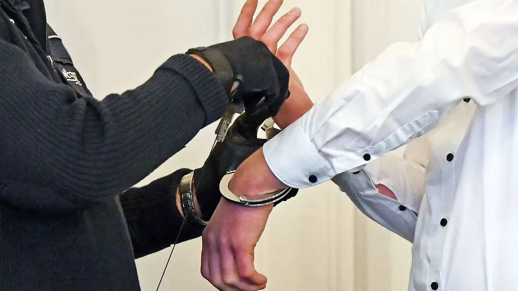 Dem-Angeklagten-in-einem-Prozess-werden-vor-Verhandlungsbeginn-im-Landgericht-Karlsruhe-die-Handschellen-abgenommen
