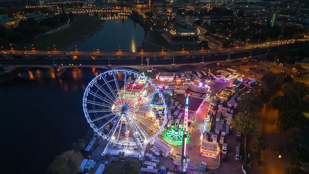 Ein-Riesenrad-und-Fahrgeschaefte-sind-am-Abend-beim-Herbstfest-auf-dem-Volksfestgelaende-Pieschner-Allee-mit-bunten-Lampen-beleuchtet