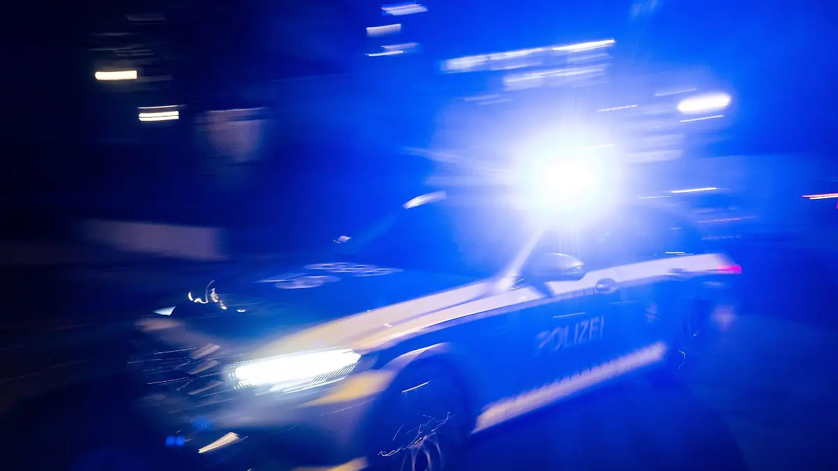 Ein-Polizeifahrzeug-faehrt-mit-Blaulicht-an-einem-Gebaeude-vorbei