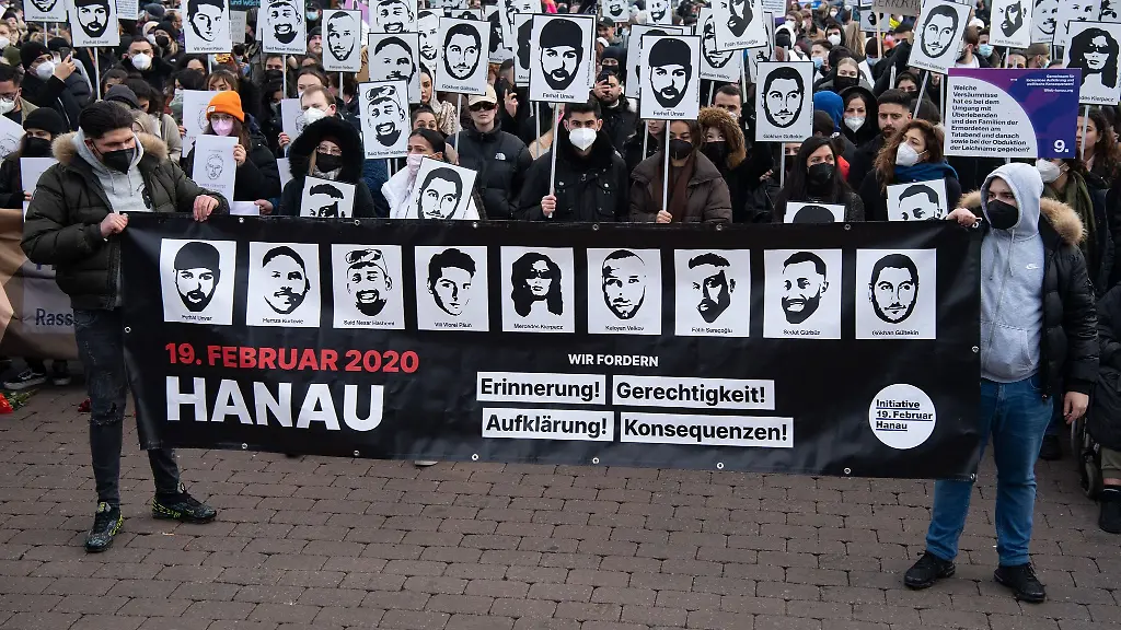 Mit-Plakaten-und-Bildern-der-Ermordeten-erinnern-Teilnehmer-einer-Gedenkveranstaltung-auf-dem-Marktplatz-von-Hanau-an-die-Opfer