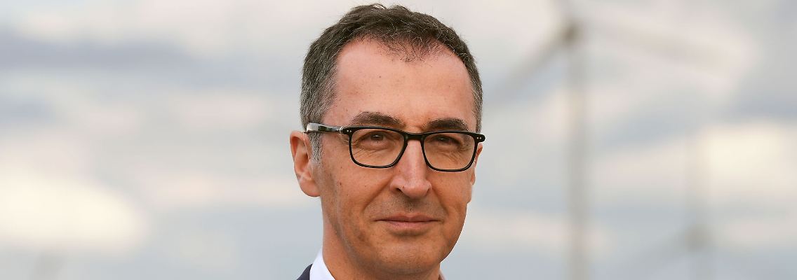 Landwirtschaftsminister Cem Özdemir (Bündnis 90/Die Grünen) steht vor einem Feld mit Weizen und Windrädern im Hintergrund.