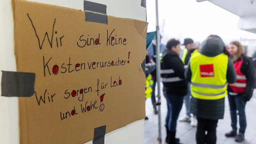 Wir-sind-keine-Kostenverursacher-Wir-sorgen-fuer-Leib-und-Wohl-steht-auf-einem-Banner