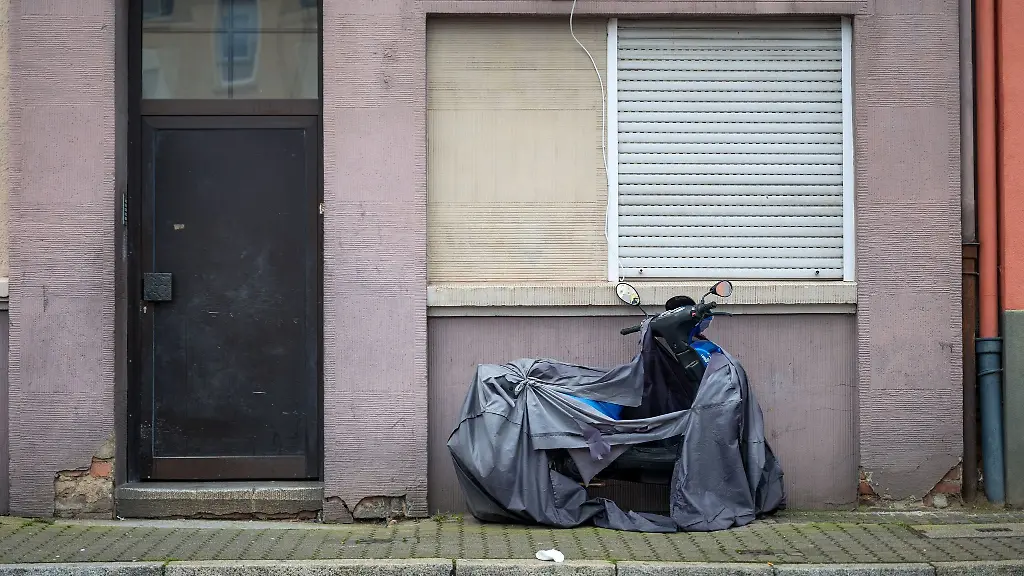 Ein-mit-einer-zerrissenen-Plane-abgedeckter-Roller-steht-vor-einem-Haus-im-Saarbruecker-Viertel-Burbach