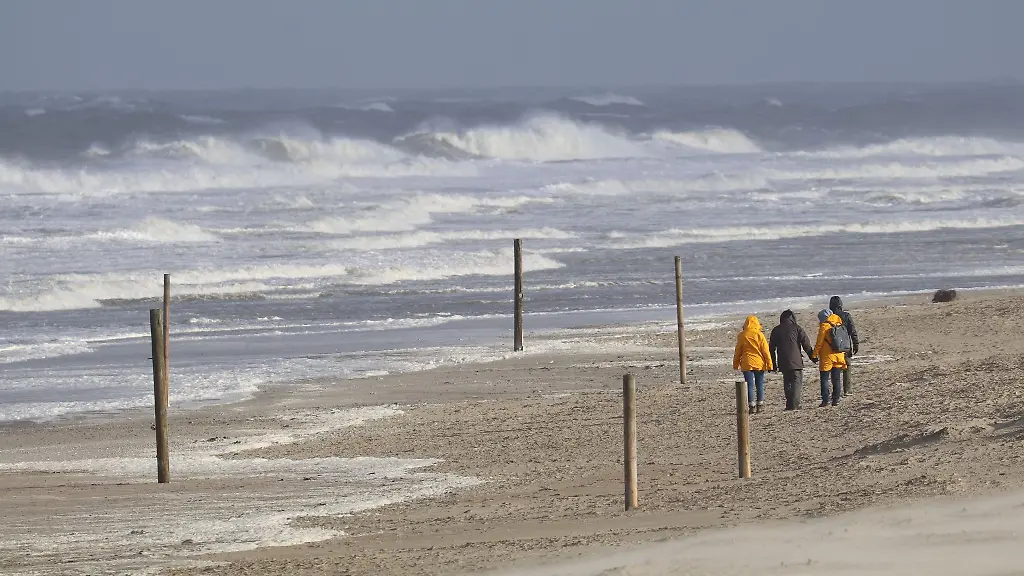 Bei-stuermischem-Wetter-und-Wellen-gehen-Spaziergaenger-am-Strand-entlang