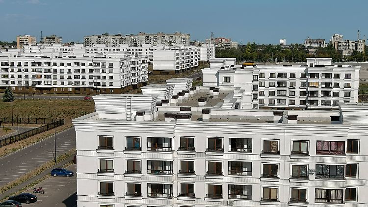 Russland hat bereits ein ganzes Viertel in Mariupol neu errichtet. Im Hintergrund teilweise zerstörte Häuser.