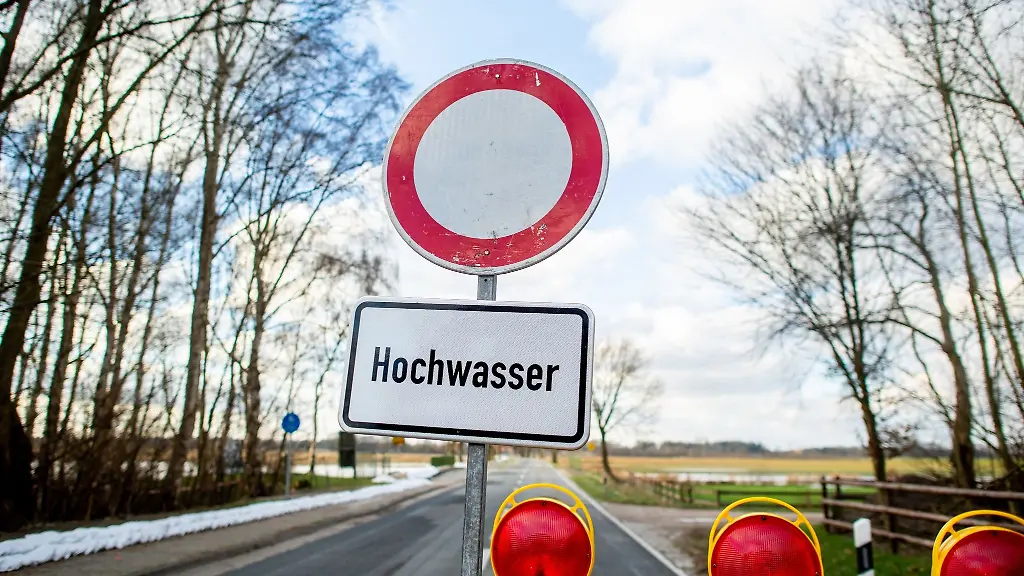 Eine-Absperrbake-und-ein-Schild-mit-der-Aufschrift-Hochwasser-steht-vor-einer-gesperrten-Strasse