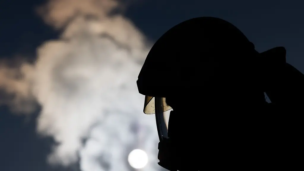 Ein-Feuerwehrmann-in-Atemschutzausruestung-steht-an-einem-Einsatzfahrzeug