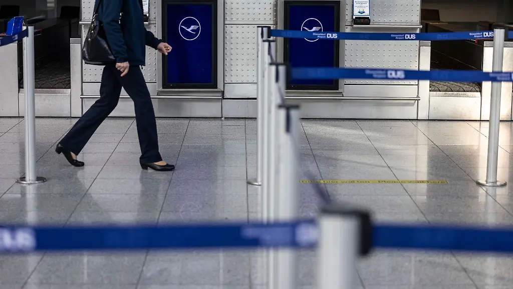 Eine-Frau-laeuft-an-Lufthansa-Schaltern-zum-Check-In-am-Flughafen-Duesseldorf-vorbei