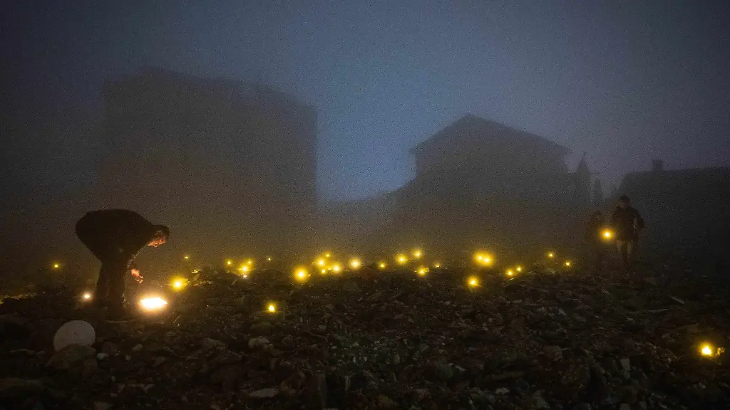 In-der-Nacht-entzuenden-Menschen-in-den-Truemmern-eines-beim-Erdbeben-zerstoerten-Hauses-Kerzen-um-an-ihre-umgekommenen-Verwandten-zu-erinnern