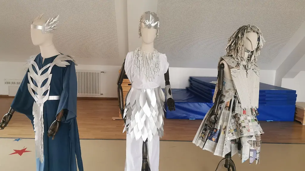 Drei-Schaufensterpuppen-tragen-Kostueme-die-aus-Materialien-bestehen-die-sonst-weggeworfen-worden-waeren-wie-alte-Zeitungen-und-Milchkartos