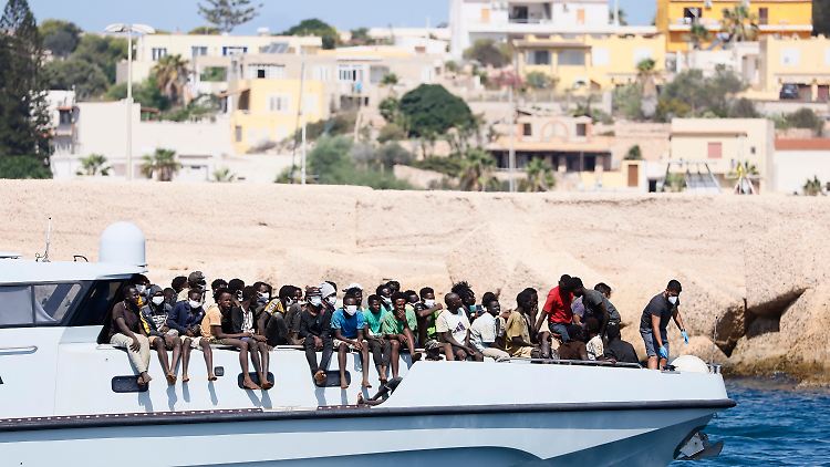 Migranten auf einem Schiff der Küstenwache - im Hintergrund: Lampedusa.