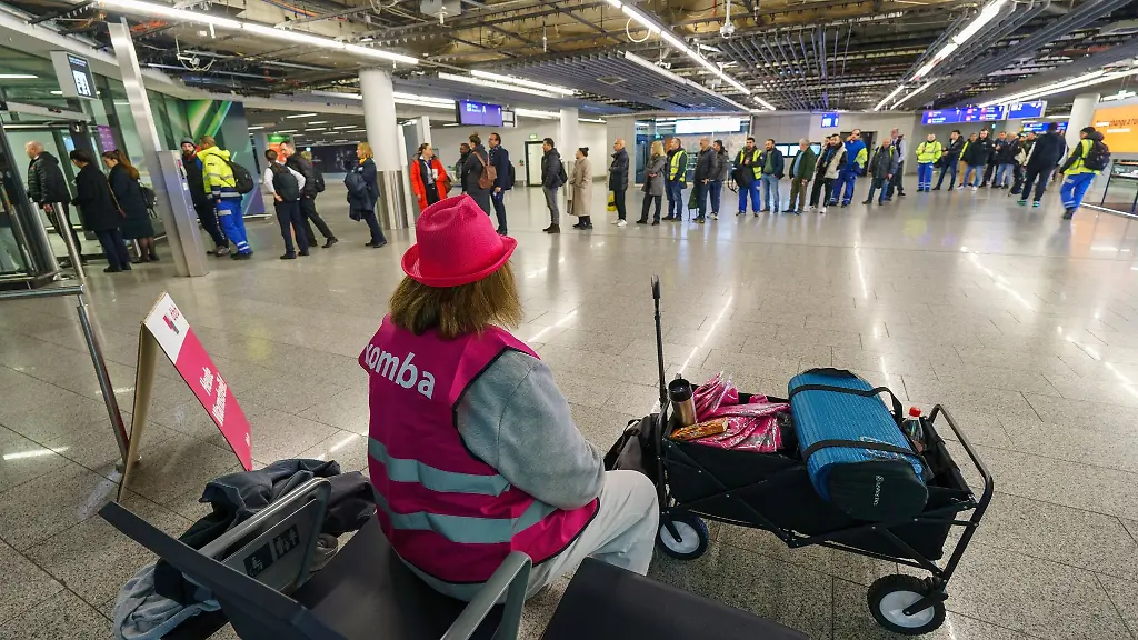 Eine-Vertreterin-der-Komba-Gewerkschaft-sitzt-am-Flughafen-waehrend-Flughafen-Beschaeftigte-zur-Sicherheitskontrolle-anstehen