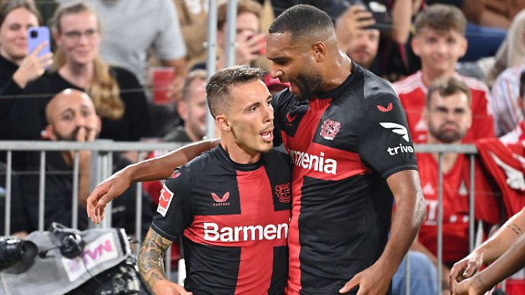 Jonathan Tah freut sich mit dem Wundertorschützen Alejandro Grimaldo. Im Hintergrund merken die Bayern-Fans, dass die Meisterchaft nur über Bayer gehen wird.  