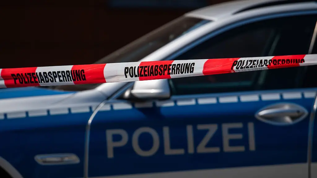 Ein-Polizeiauto-steht-hinter-einem-Absperrband-der-Polizei
