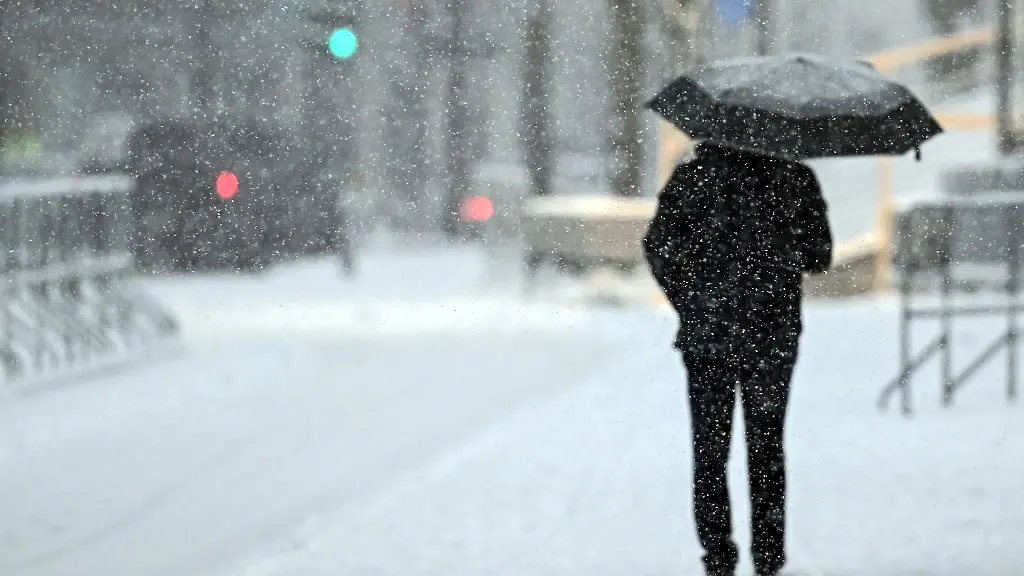 Ein-Fussgaenger-geht-mit-einem-Schirm-durch-das-Schneetreiben-in-Koeln