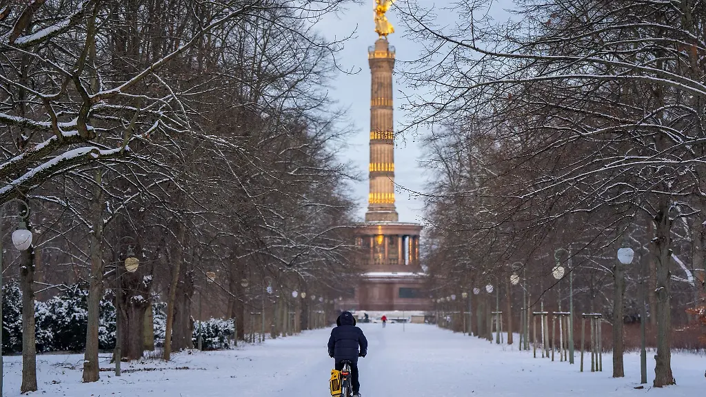 Eine-Mann-faehrt-auf-dem-Fahrrad-vor-der-Kulisse-der-Siegessaeule-durch-den-verschneiten-Tiergarten