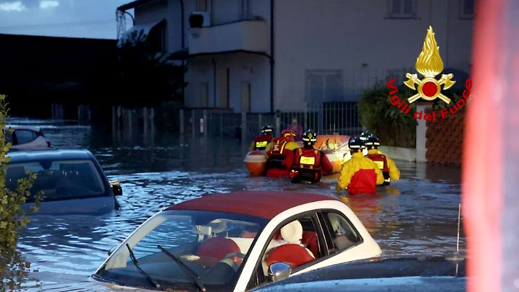 Feuerwehrleute schieben ein Schlauchboot durch eine überschwemmte Straße in der Toskana.