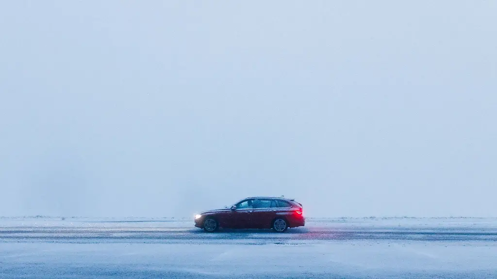 Ein-Auto-faehrt-bei-dichtem-Nebel-ueber-eine-schneebedeckte-Strasse