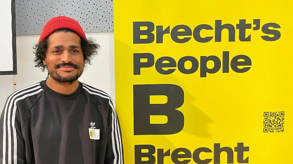 Julian-Warner-Leiter-des-Brechtfestivals-in-Augsburg-steht-neben-einem-Banner-des-Brechtfestivals-2023