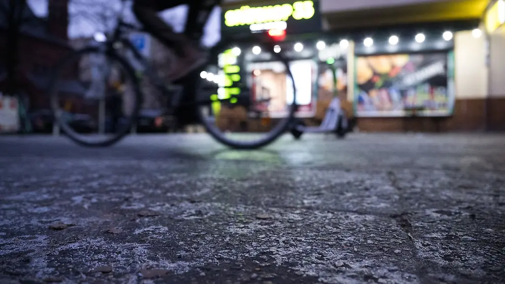 Ein-Fahrradfahrer-faehrt-auf-einem-Fahrradweg-mit-einer-duennen-Eisschicht-entlang