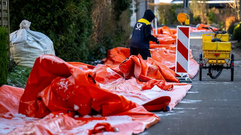 Eine-Postbotin-steigt-ueber-den-mobilen-Deich-der-nun-wieder-abgebaut-wird