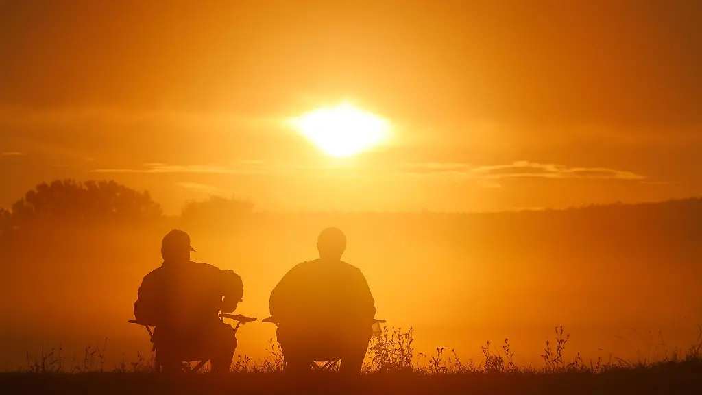 Zwei-Angler-sitzen-auf-Campingstuehlen-und-schauen-sich-den-Sonnenaufgang-an