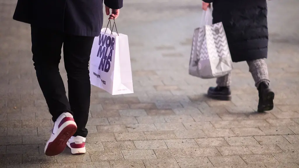 Eine-Passantin-und-ein-Passant-laufen-mit-Einkaufstaschen-durch-die-Innenstadt