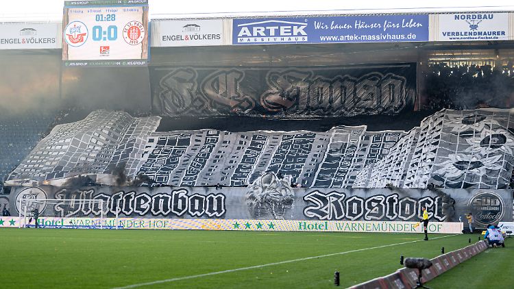 Unter dem riesigen Banner mit dem Sonnenblumenhaus in Rostock-Lichtenhagen strömt schwarzer Rauch hervor.