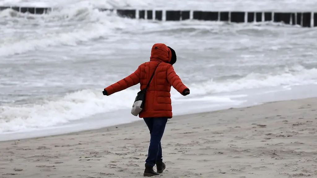 Eine-Spaziergaengerin-geht-bei-Wind-und-Regen-ueber-einen-Strand