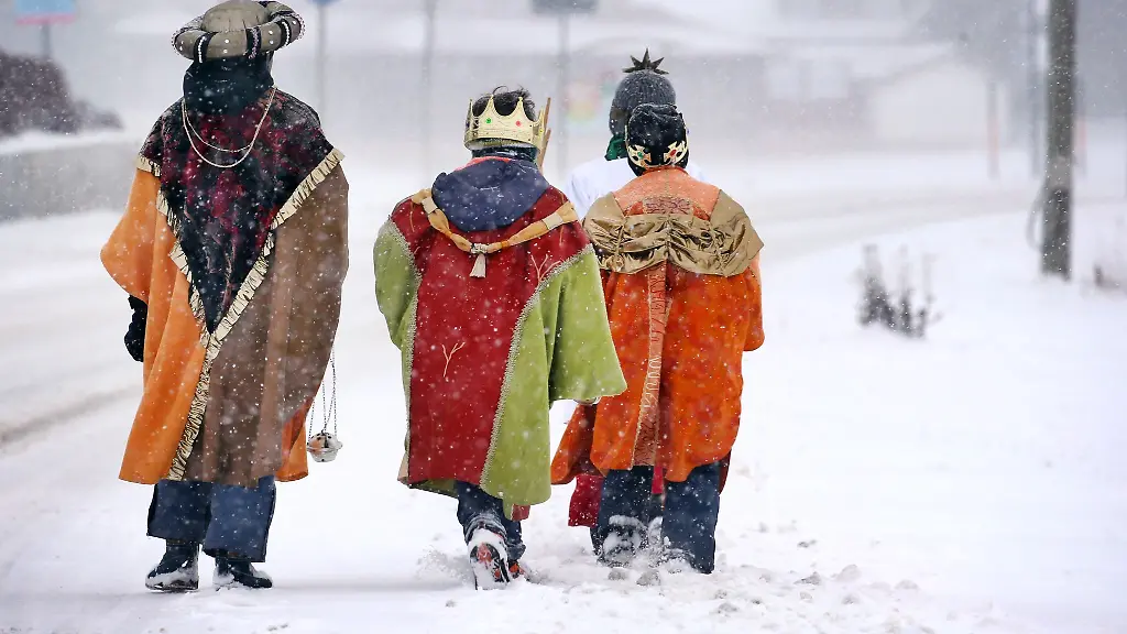 Sternsinger-gehen-im-dichten-Schneetreiben-in-ihren-bunten-Kostuemen-an-einer-Strasse-entlang