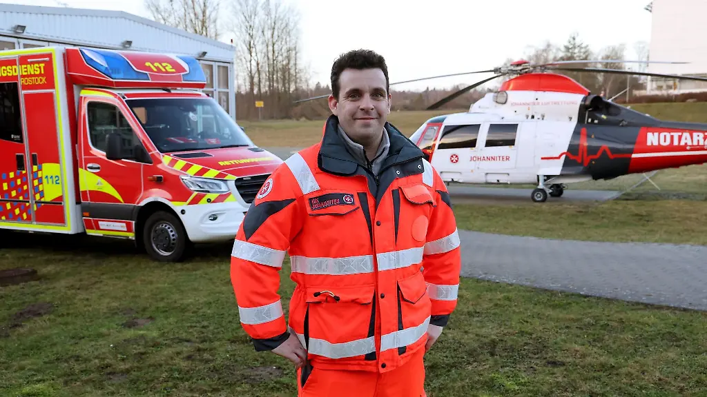 Christian-Manshen-Notfallsanitaeter-bei-der-Johanniter-Unfall-Hilfe-e-V-steht-vor-Rettungswagen-und-Rettungshubschrauber