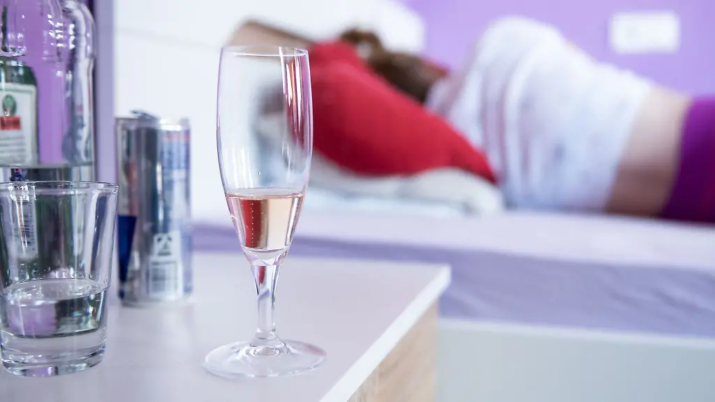 Eine-Frau-liegt-in-ihrem-Bett-neben-dem-Flaschen-und-Glaeser-mit-Alkohol-stehen
