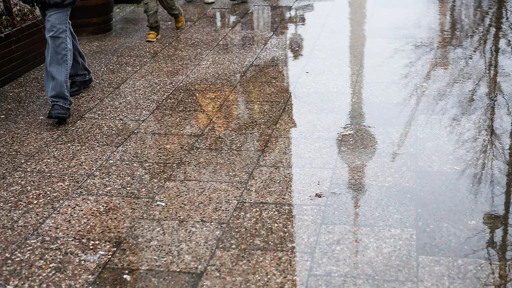 Passanten-gehen-an-einer-Pfuetze-vorbei-in-der-sich-der-Fernsehturm-spiegelt
