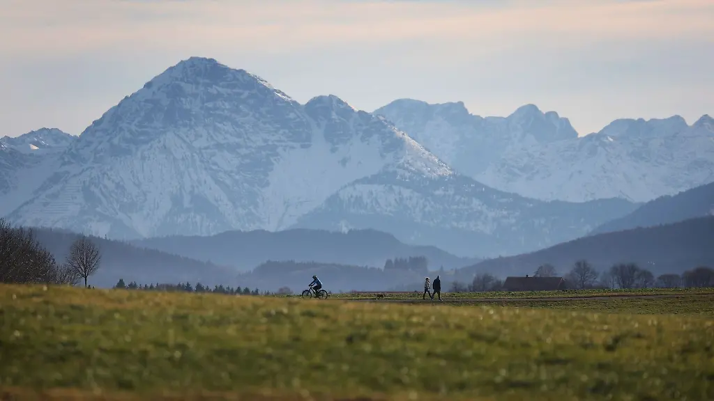 Spaziergaenger-gehen-neben-einem-Radfahrer-im-Sonnenschein-vor-den-Alpen