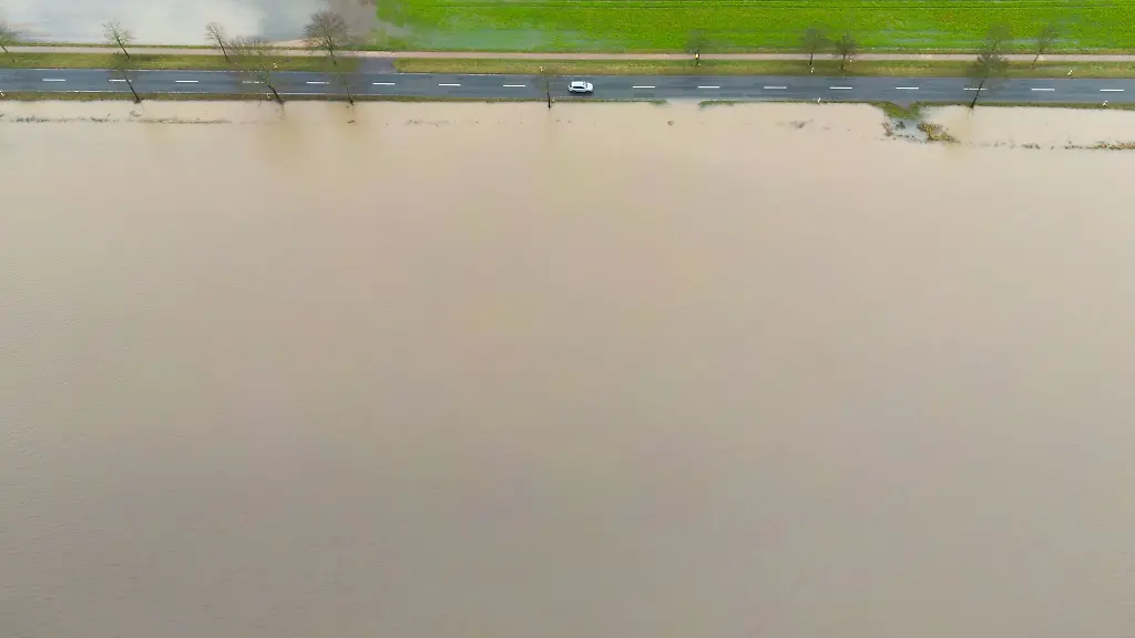 Ein-Auto-faehrt-neben-einem-ueberfluteten-Feld-ueber-eine-Landstrasse